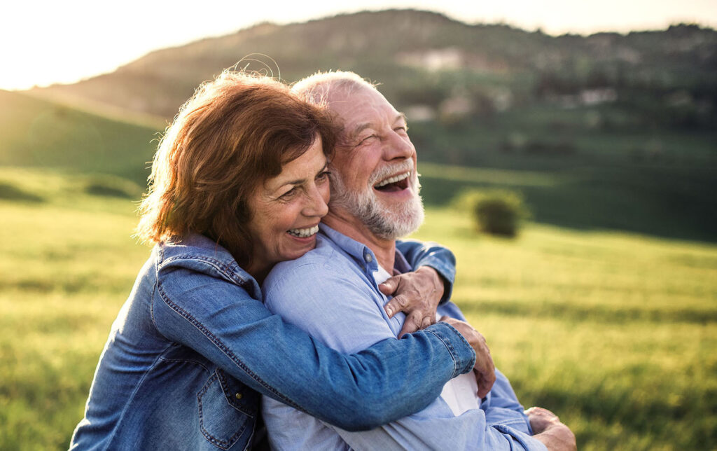 Happy older couple smiling outdoors after implant-supported denture treatment